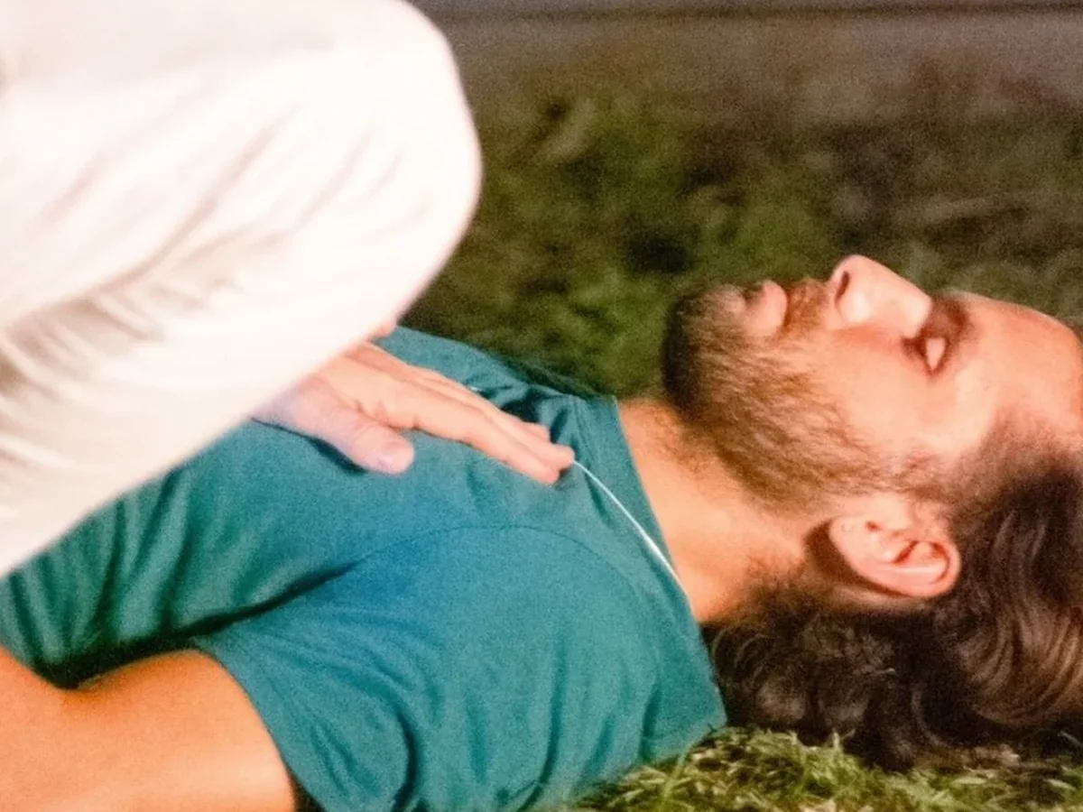 Jeff's hand on a man's chest as he lies on the grass